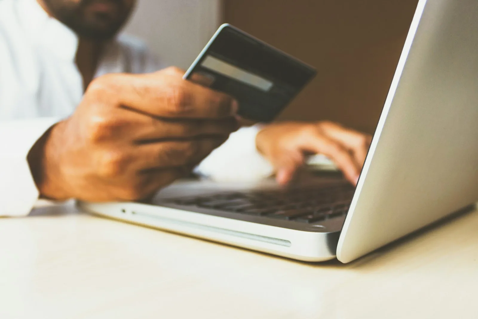 Persona comprando en una tienda online desde un portátil, con la tarjeta de crédito en la mano